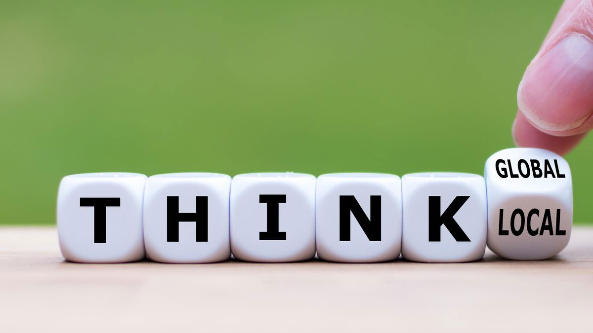 A hand points to a dice spelling "think global, act local" with the last dice tipped over.