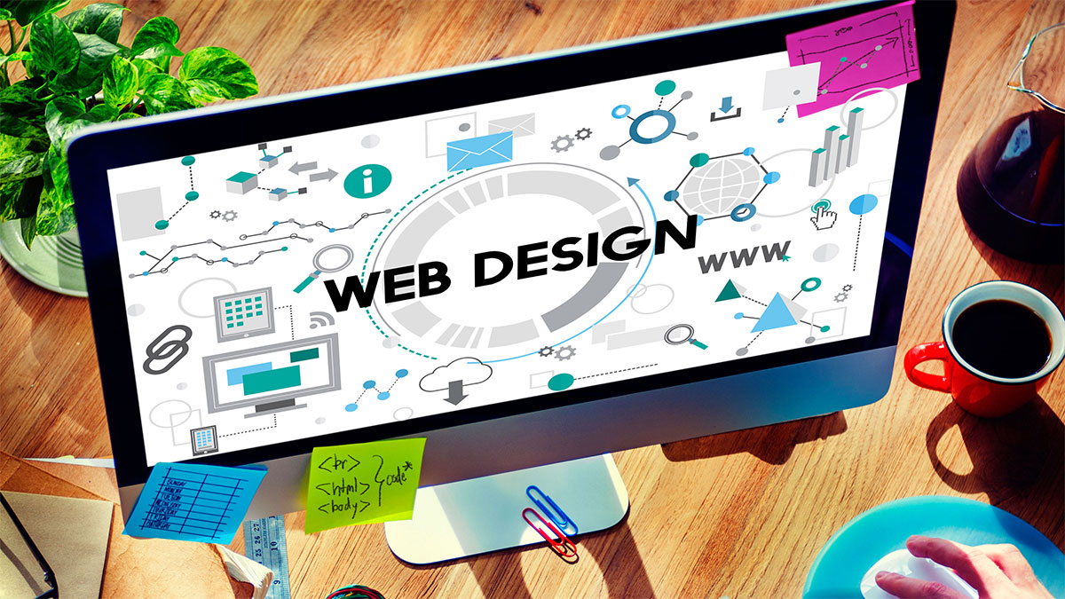 A workspace showing a computer screen displaying web design elements, surrounded by notes, a coffee cup, and design tools.
