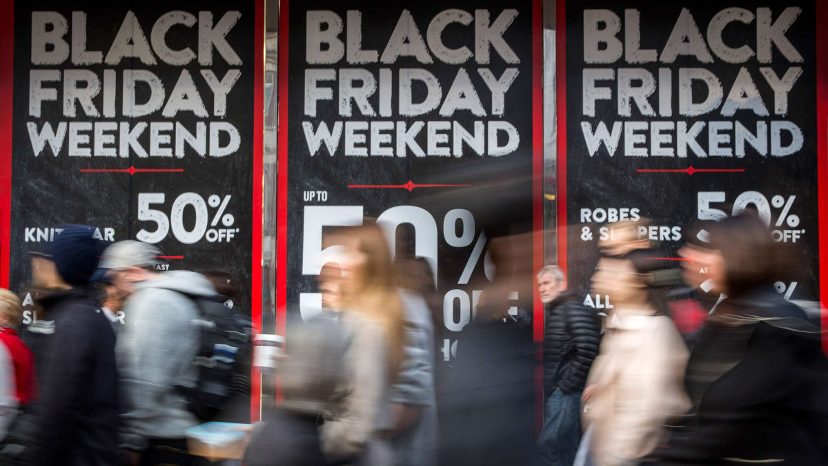 Busy shoppers pass by storefronts advertising Black Friday weekend sales with up to 50 percent off various items.